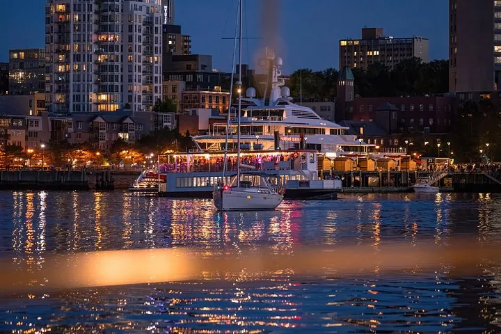 Bateaux et yachts illuminés dans un port la nuit avec les lumières de la ville.